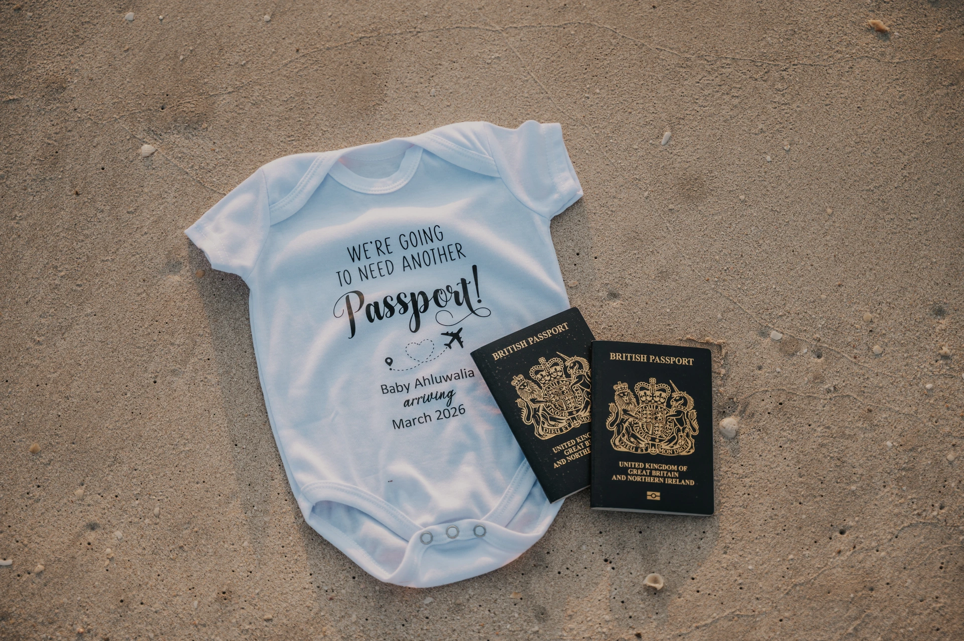 White baby onesie and two passports on beach sand in Dubai, styled prop setup for a maternity session.