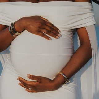 Close-up of pregnant woman in white dress holding belly during maternity photoshoot on Dubai beach