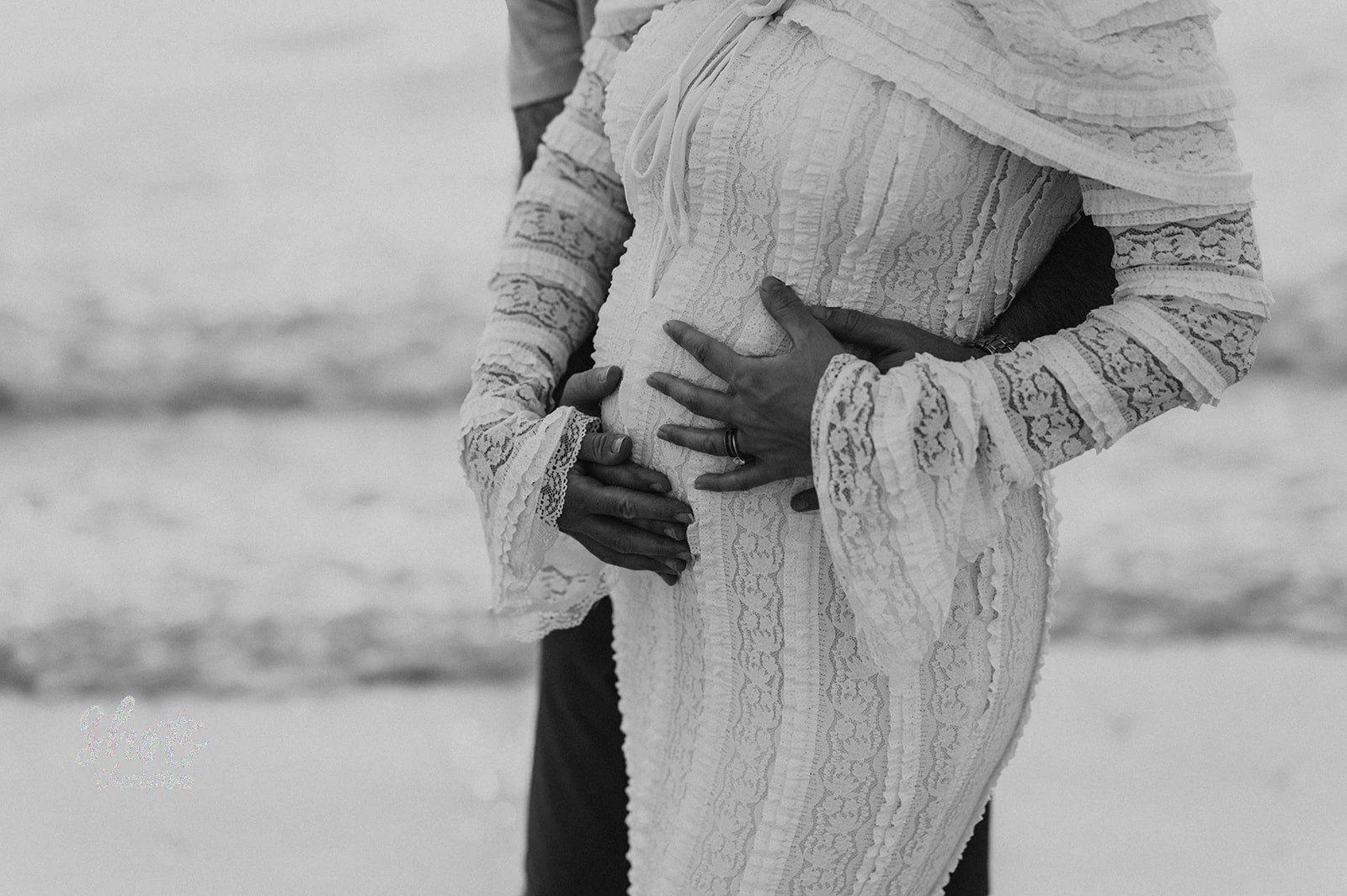 Close-up of couple’s hands on pregnant belly during maternity photoshoot on Dubai beach