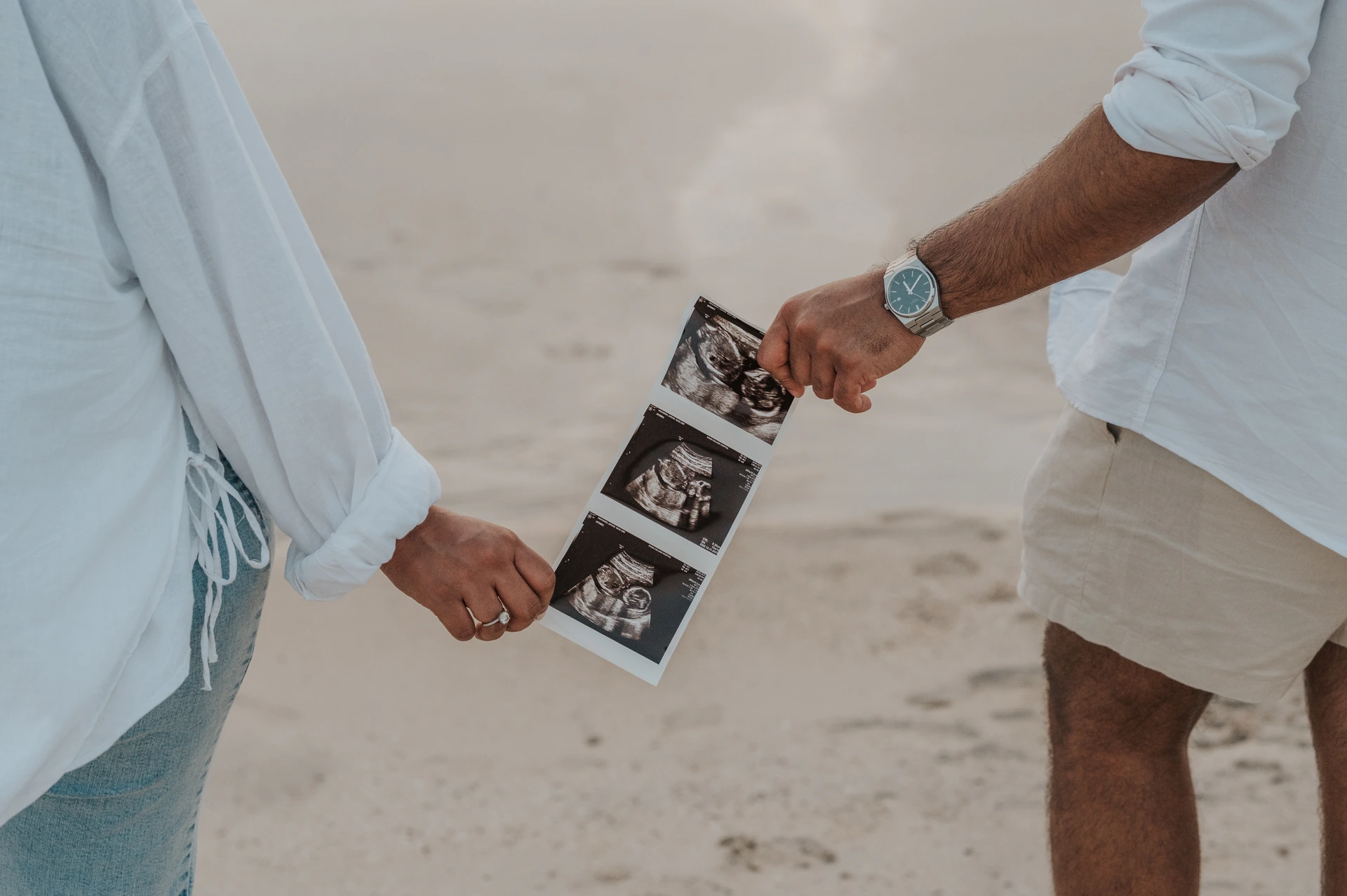 An expectant couple holds a strip of ultrasound photographs between them on the sand during a Dubai maternity session.