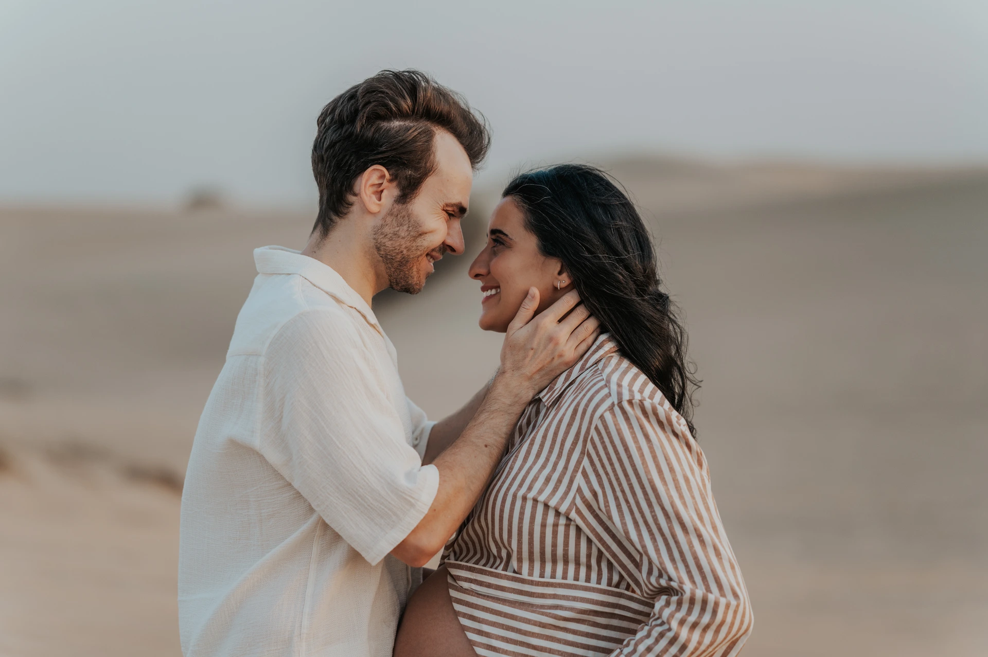 Dubai Desert Maternity Couple Face-to-Face An expectant couple smiles face-to-face while standing close together on the dunes during a Dubai desert maternity photoshoot.