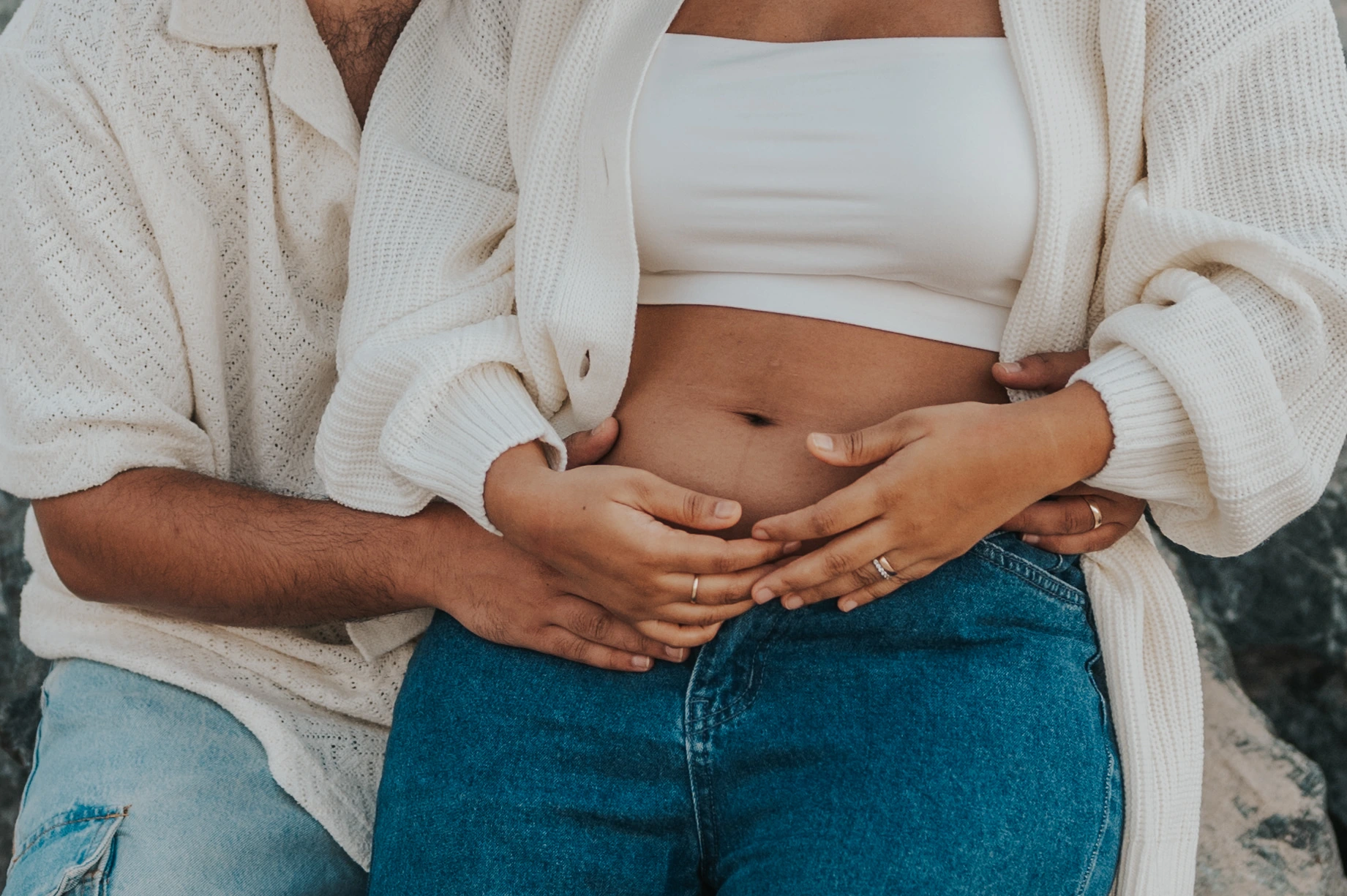 An expectant couple layers their hands around a bare bump during a close-up Dubai beach maternity portrait.