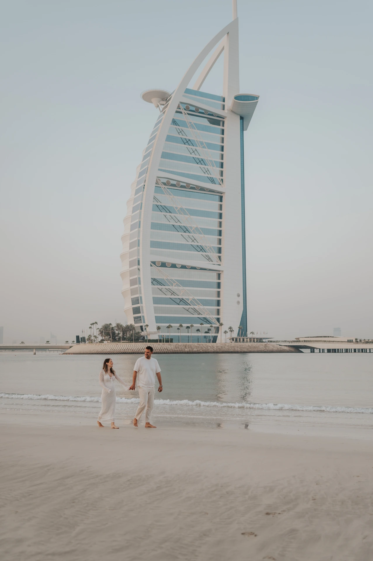An expectant couple walks along the beach beneath Burj Al Arab during their landmark Dubai maternity photoshoot.