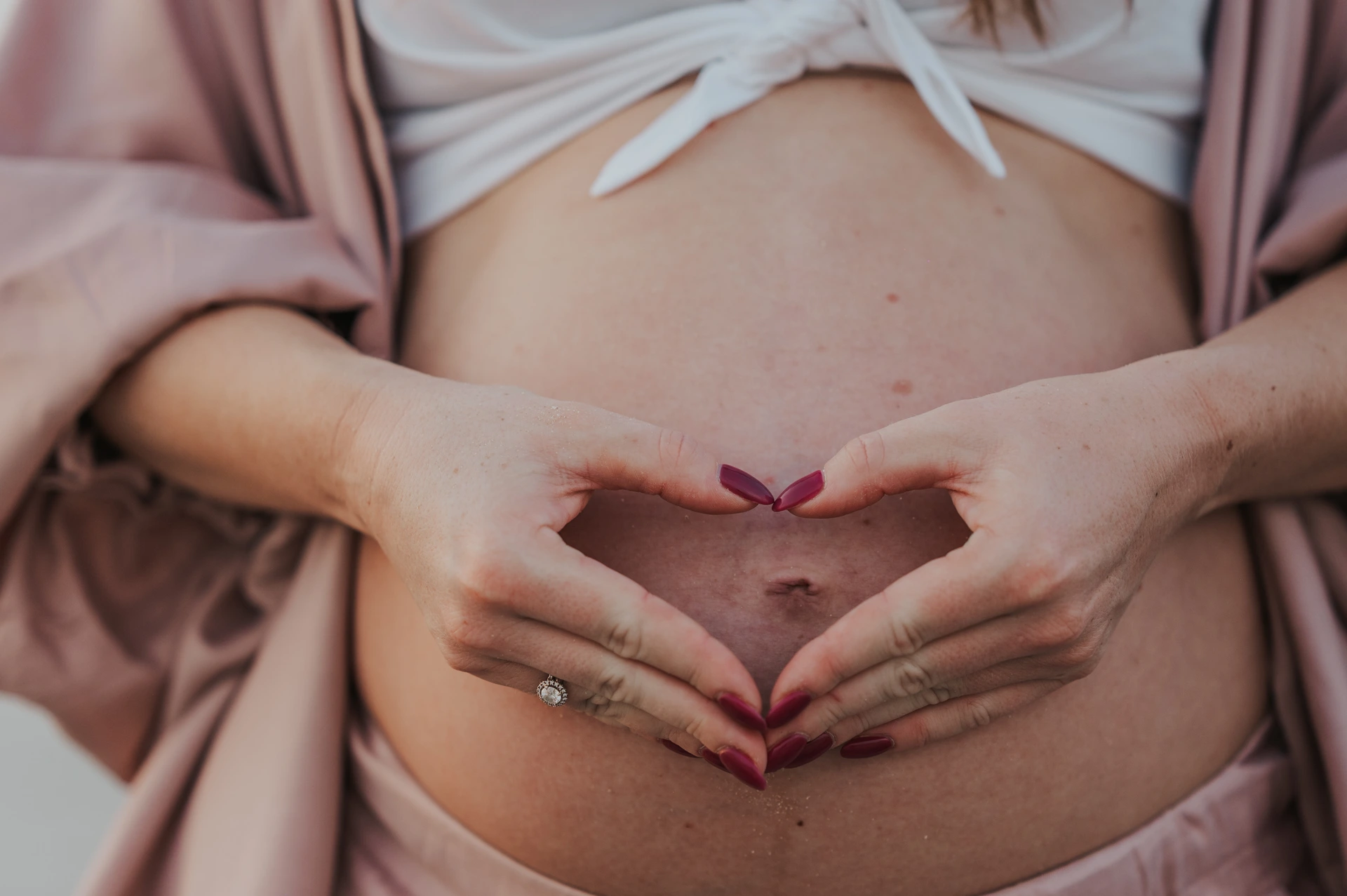 Dubai Beach Maternity Heart Hands on Bump A pregnant woman forms a heart with her hands over her bare bump during a close-up Dubai maternity portrait.