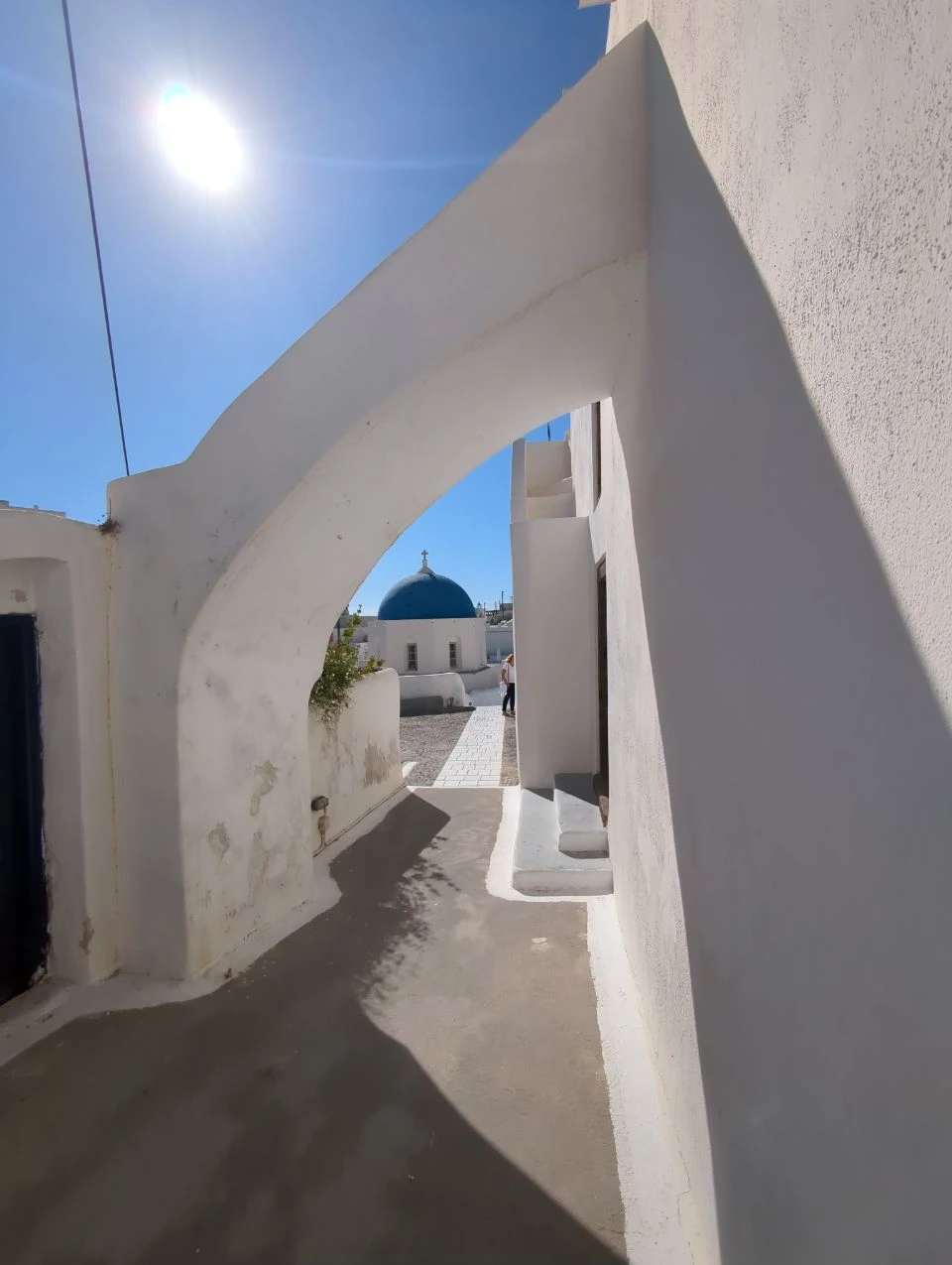 Megalochori arch with sun and shade | Santorini daytime photos Sunlit white arch framing a blue dome beyond a shaded Megalochori lane
