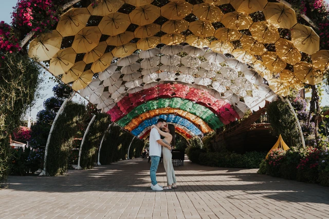A couple stands and embraces under a colorful floral tunnel in Dubai Miracle Garden during a romantic photoshoot.