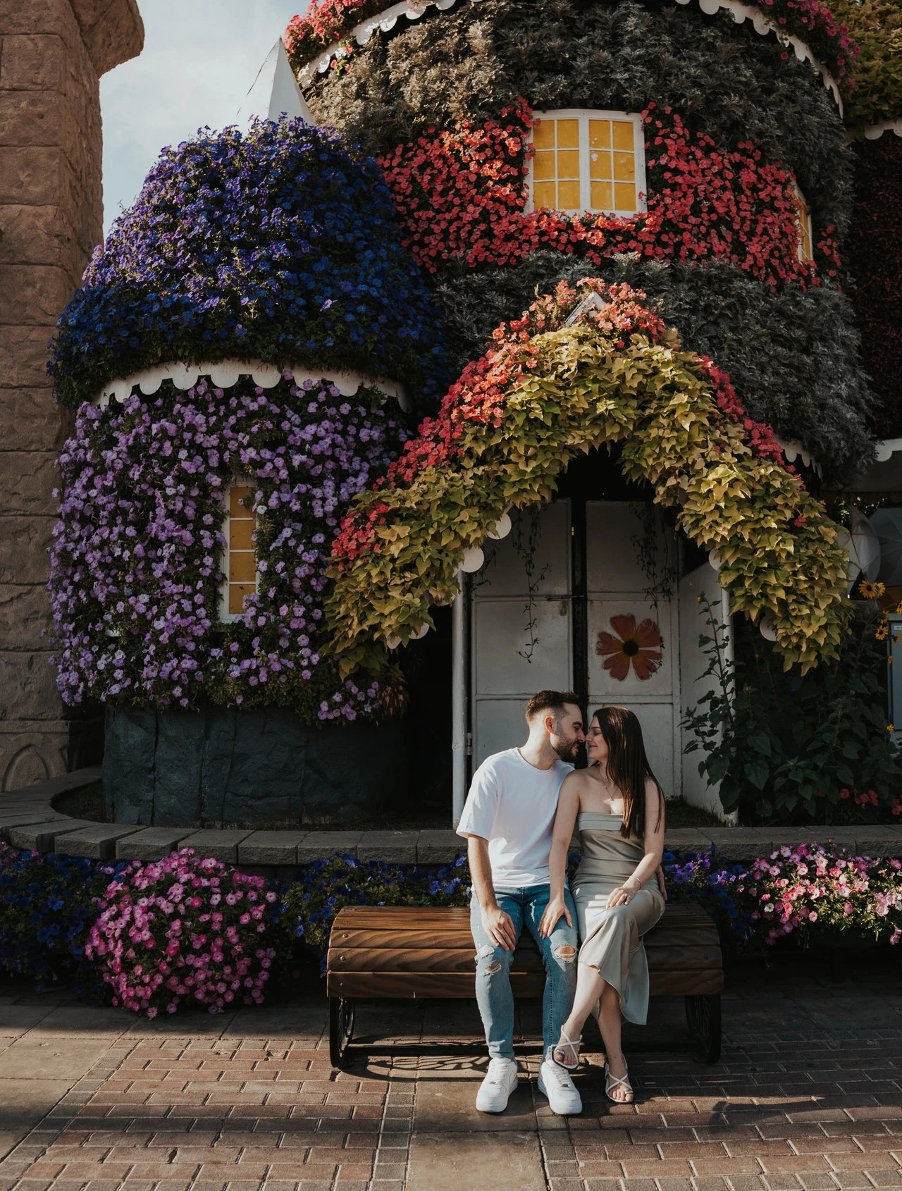 A couple stands near a flower-draped cottage doorway in Dubai Miracle Garden during an intimate couple photoshoot.