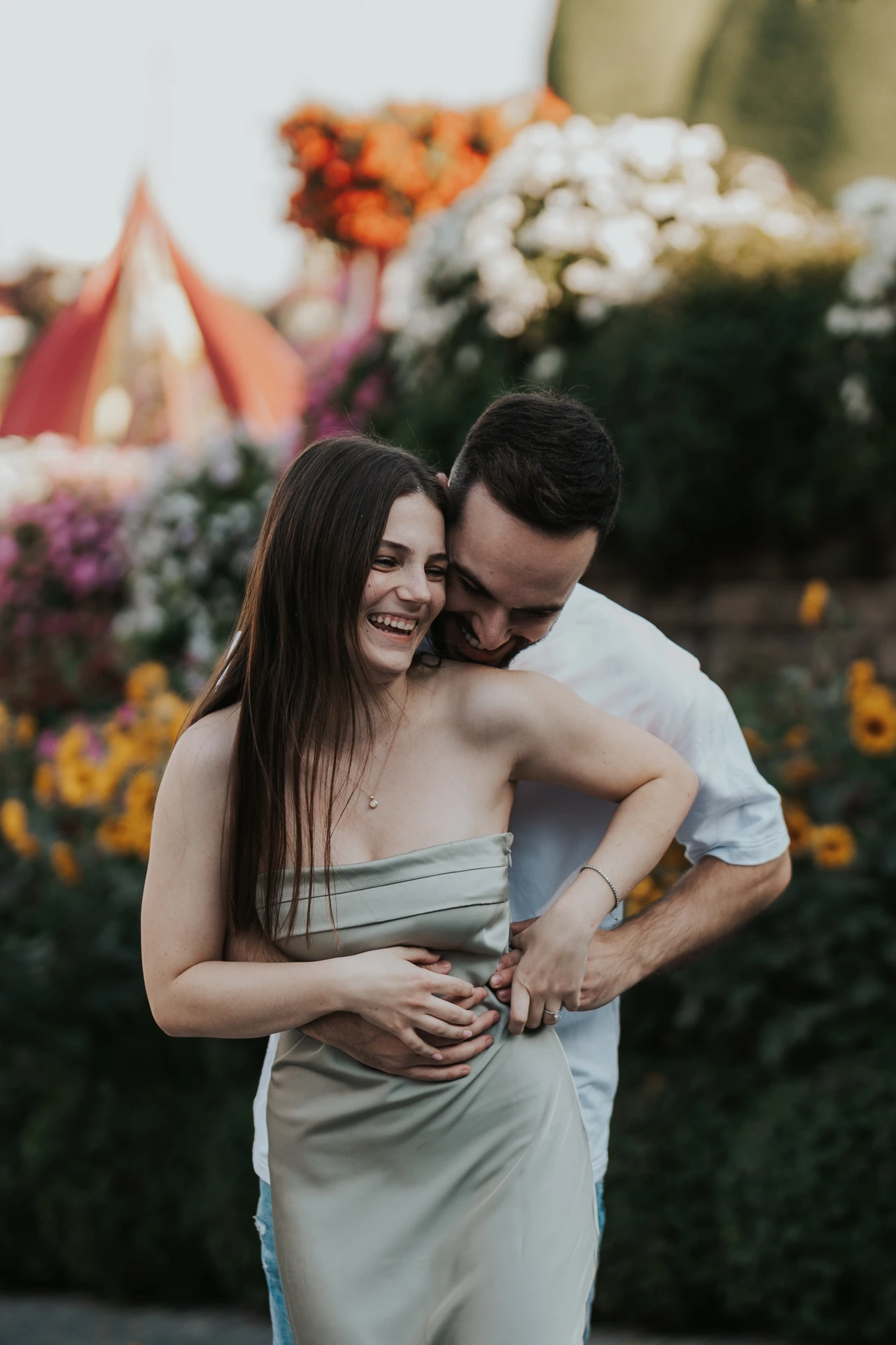 Close portrait of a couple embracing and laughing among colorful flowers in Dubai Miracle Garden during a photoshoot.