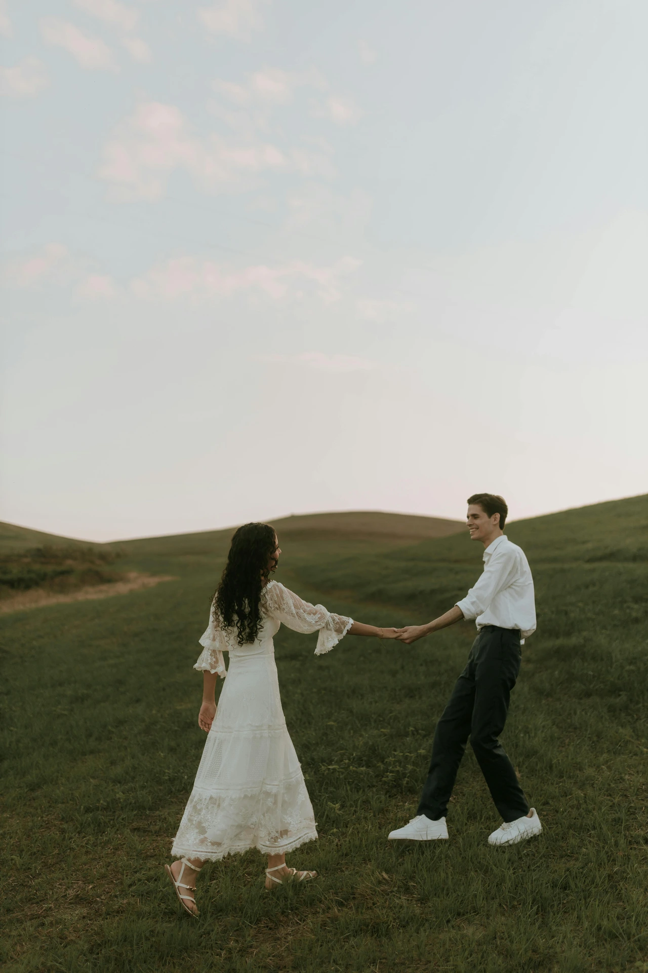 Mountain engagement outfits with layers Couple walking through green hills in layered engagement outfits