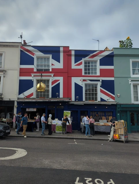 Union Jack painted across a Portobello Road shopfront above outdoor displays and passing shoppers