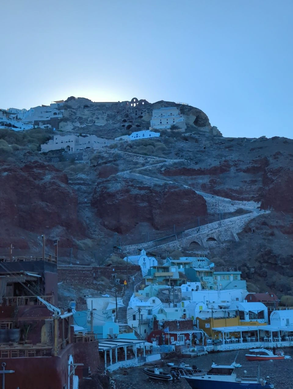Stone steps winding down from Oia Castle to the boats and waterfront buildings of Ammoudi harbour