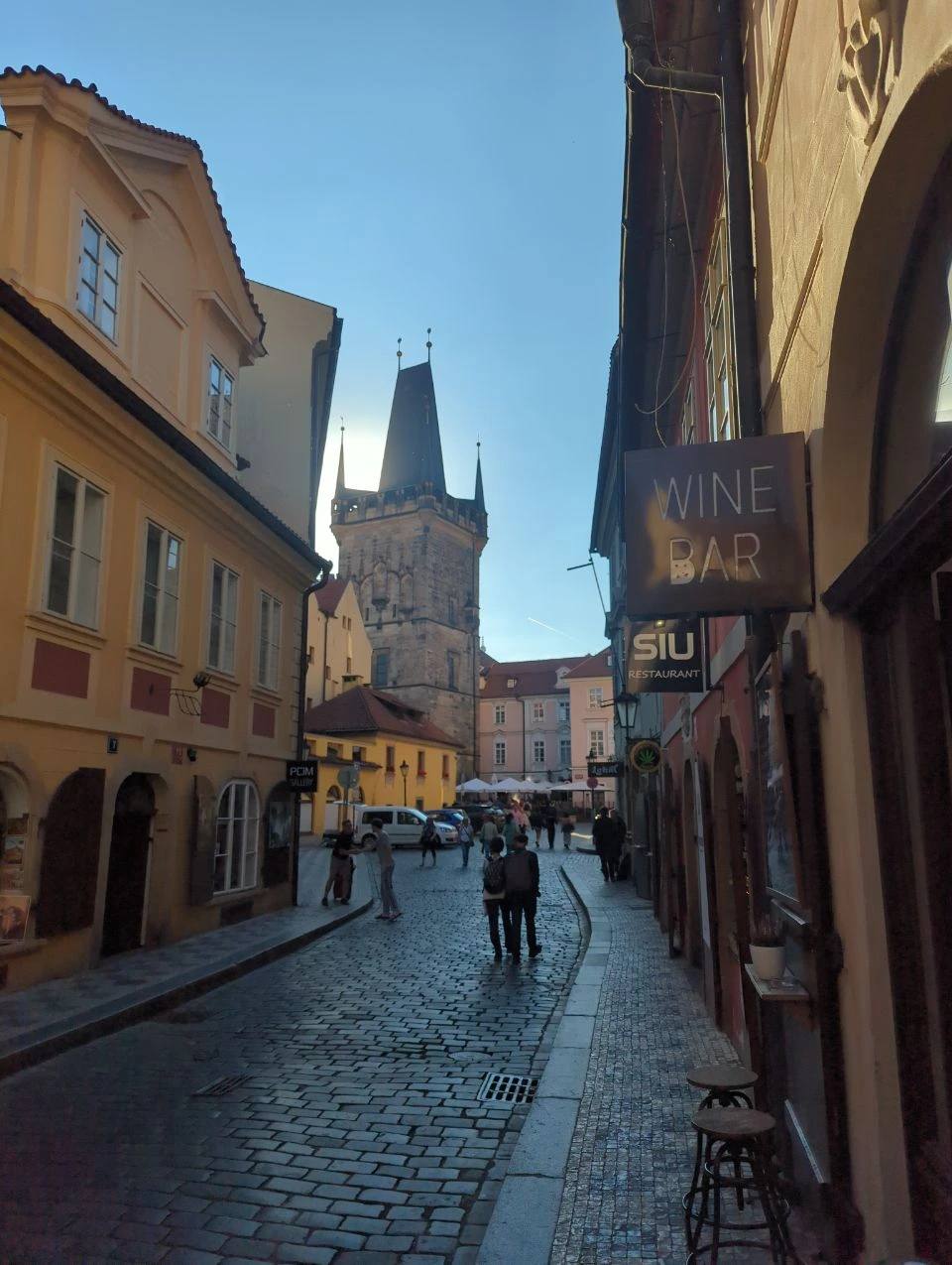 Malá Strana Photos - Prague Street and Tower A cobbled Malá Strana street leads towards a Charles Bridge tower between colourful Prague façades.