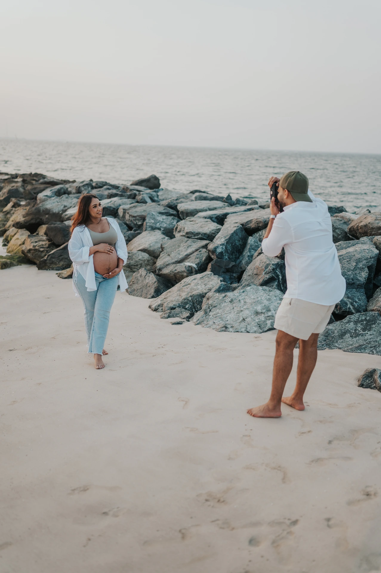 A photographer captures a pregnant subject near Dubai shoreline rocks during a maternity shoot, showing how outfit color and contrast read on camera.