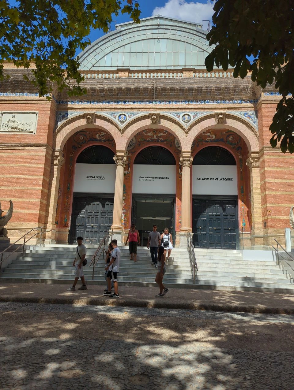 Retiro Photoshoot - Palacio de Velázquez Entrance Visitors cross the steps beneath brick arches and colourful tilework at Palacio de Velázquez in Madrid's Retiro Park.