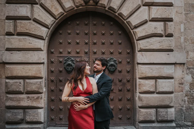 Sesión de Fotos Barcelona 30 Minutos - Portal del Barrio Gótico Una pareja se abraza ante un portal de madera ornamentado en el Barrio Gótico de Barcelona durante una sesión de fotos de 30 minutos en Barcelona.