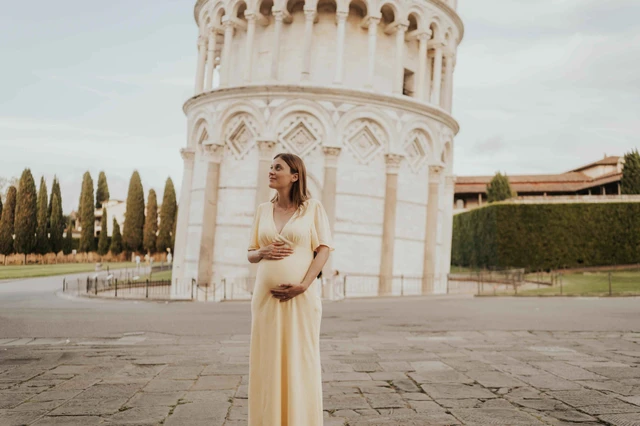 Maternity portrait of a woman in a yellow dress beside the Leaning Tower of Pisa