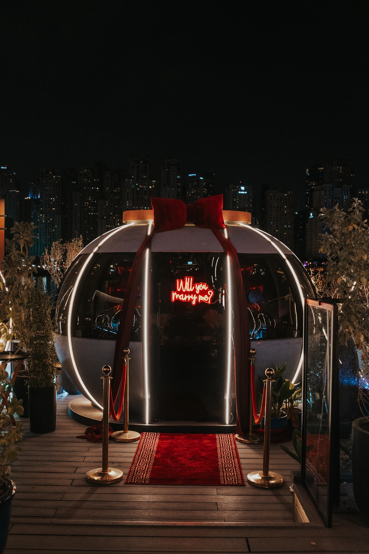 The entrance to The Pods in Dubai decorated with red drapes, a red carpet, and a glowing “Will you marry me?” sign at night.
