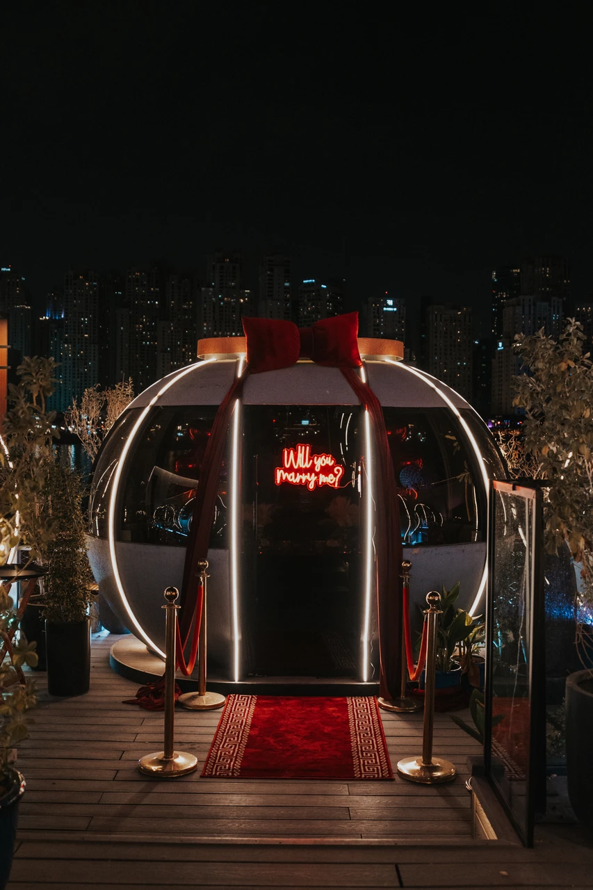 Proposal at the Pods in Dubai - Nighttime pod entrance The entrance to The Pods in Dubai decorated with red drapes, a red carpet, and a glowing “Will you marry me?” sign at night.