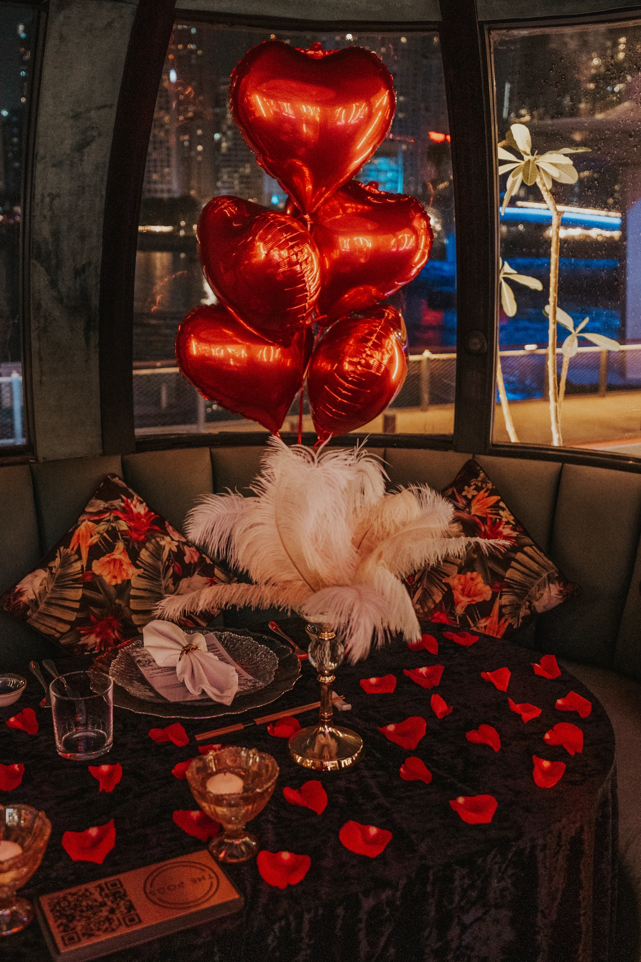 A romantic proposal dinner table setup inside The Pods in Dubai with heart-shaped red balloons, rose petals, and candlelight.