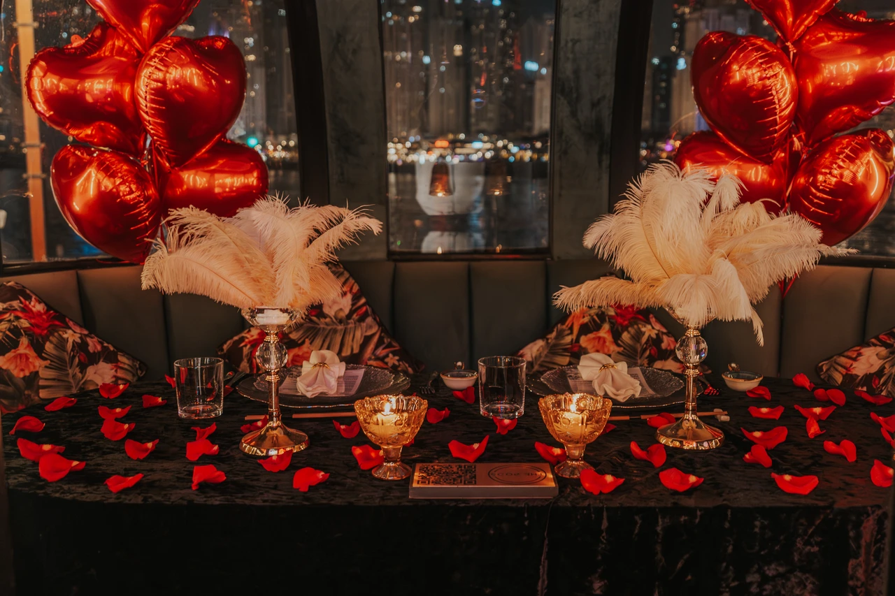 Proposal at the Pods in Dubai - Two-seat celebration table A two-seat proposal dinner setup in The Pods with red balloons, rose petals, and marina lights visible through the windows.