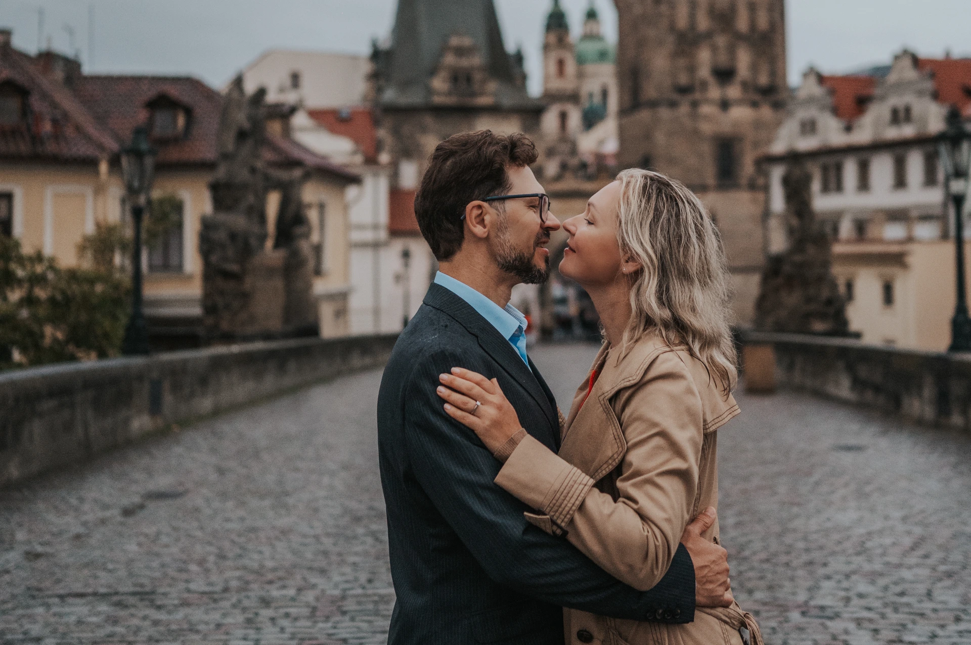 Close landscape portrait of the couple kissing, with the bridge towers in the background, on their Prague anniversary photoshoot.