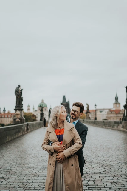 Prague anniversary photoshoot with an embrace on Charles Bridge Couple embracing on wet Charles Bridge cobblestones during their anniversary photoshoot in Prague.