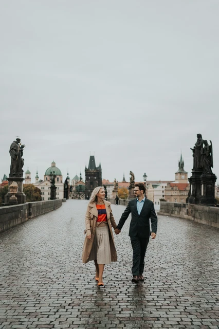 Couple walking hand in hand between the statues of Charles Bridge during a Prague anniversary photoshoot.