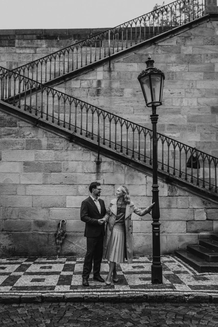 Black-and-white Prague couple photoshoot beside Charles Bridge Black-and-white portrait of the couple beside a lamppost and stone staircase on their Prague anniversary photoshoot.