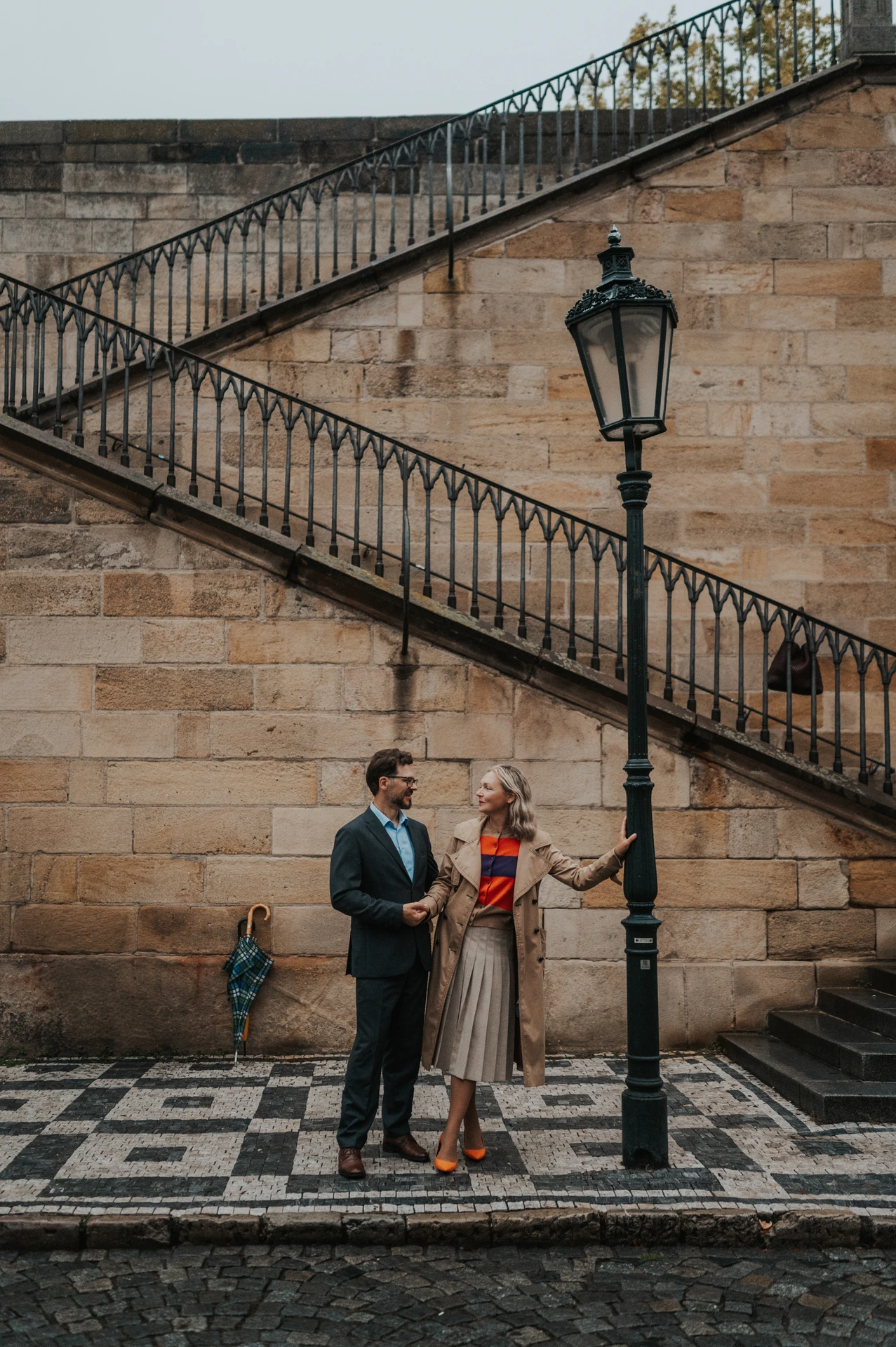 Couple standing beside an old lamppost beneath the Charles Bridge stairs during a Prague anniversary photoshoot.