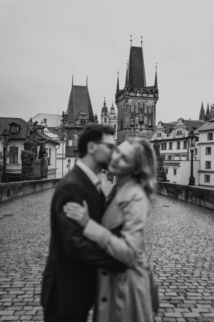 Black-and-white Prague anniversary photoshoot with the bridge towers Black-and-white photograph with the kissing couple softly blurred and Charles Bridge towers behind them on their Prague photoshoot.