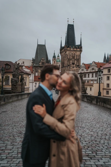 Prague couple photoshoot with the bridge towers in focus Soft-focus couple kissing in the foreground with the Charles Bridge towers in focus during a Prague anniversary photoshoot.
