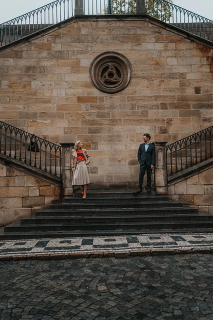 Couple standing apart beside the symmetrical stair railings at Charles Bridge on their Prague anniversary photoshoot.