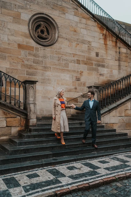 Prague couple photoshoot walking down the Charles Bridge steps Couple holding hands as they step down the Charles Bridge stairs during their anniversary photoshoot in Prague.