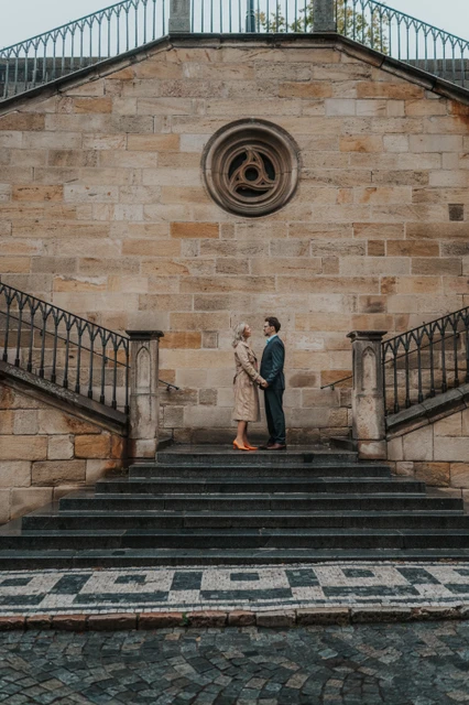 Prague couple photoshoot on the Charles Bridge staircase Couple standing together on the stone staircase beside Charles Bridge during an anniversary photoshoot in Prague.