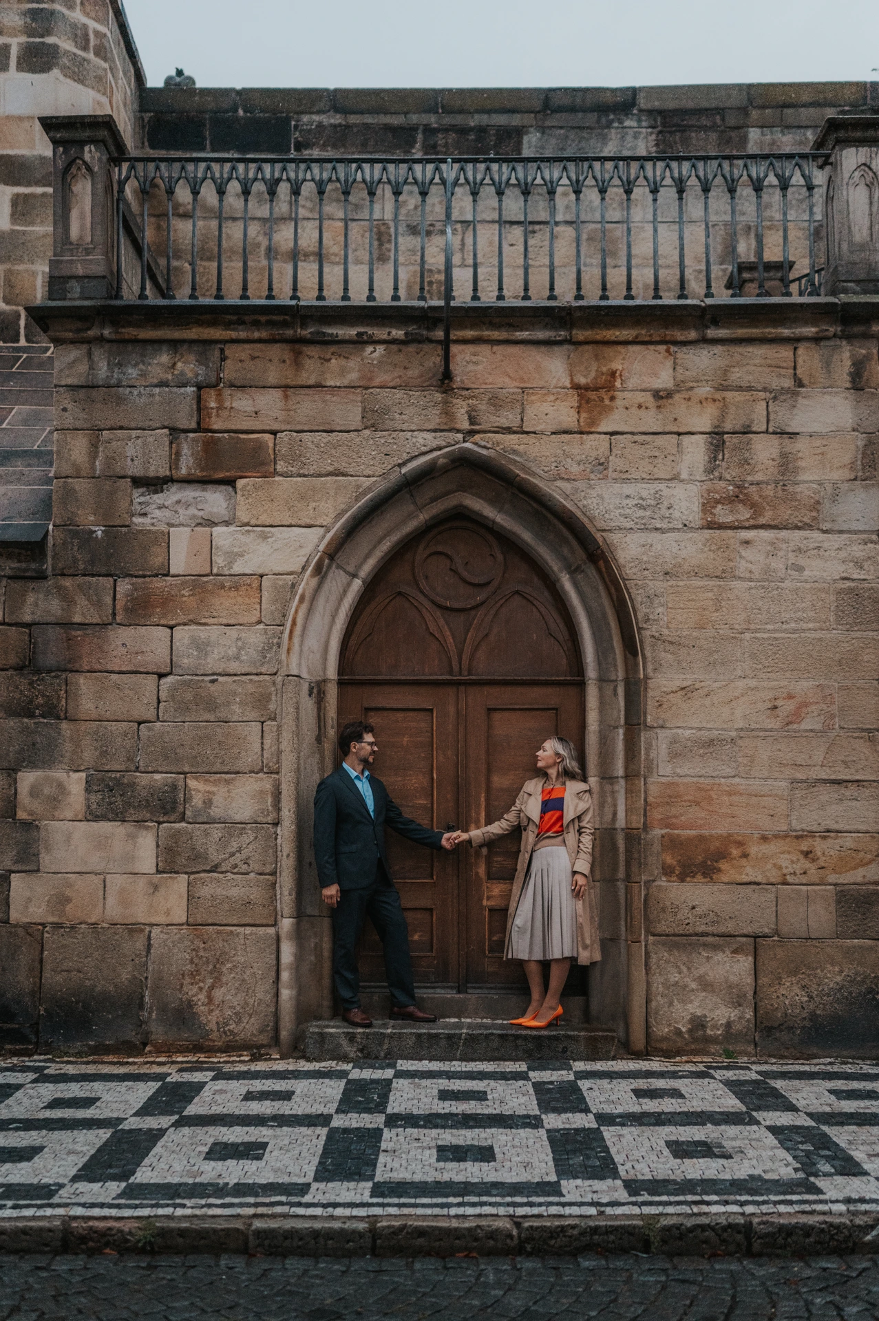 Couple holding hands across an arched wooden doorway beneath Charles Bridge during their Prague anniversary photoshoot.