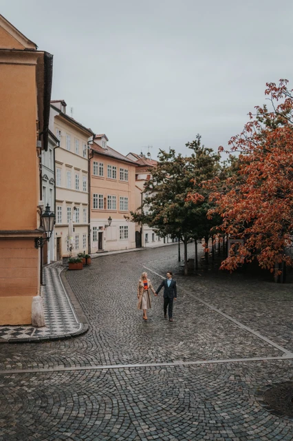 Prague anniversary photoshoot among Kampa's colourful houses Couple holding hands on a cobbled Kampa street below colourful houses during their anniversary photoshoot in Prague.