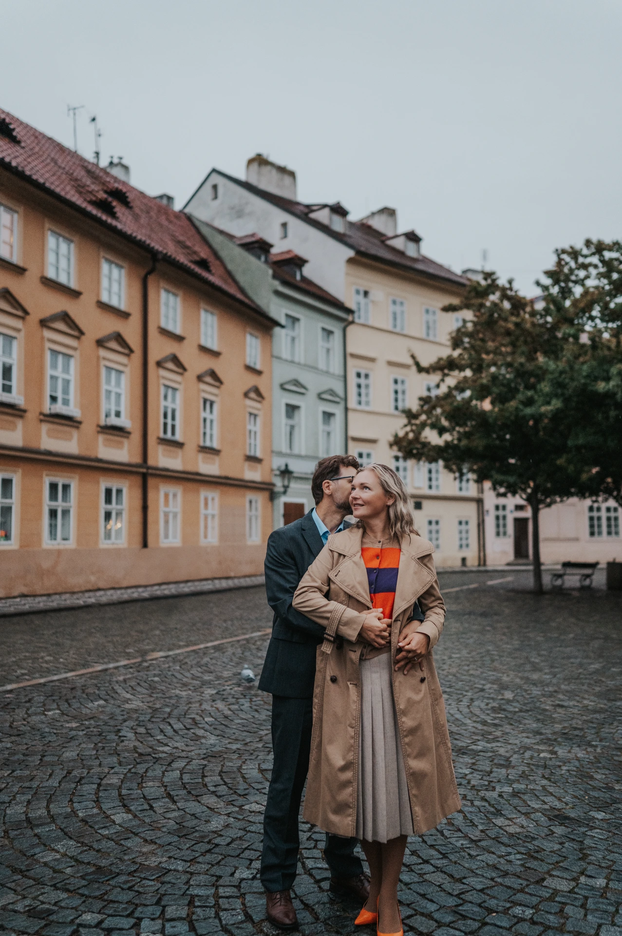 Couple sharing an embrace in front of Kampa's yellow houses during their anniversary photoshoot in Prague.