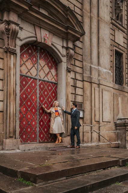 Couple holding hands while stepping away from the red Old Town doorway during their Prague anniversary photoshoot.