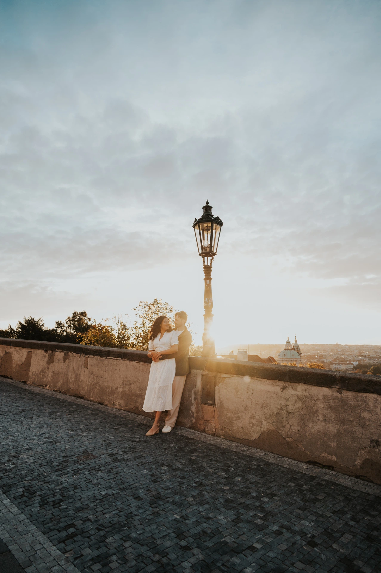 Couple holding each other beside a street lamp at the viewpoint during an anniversary couple photoshoot in Prague.