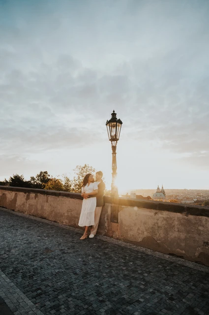 Prague anniversary photoshoot: couple holding each other beside a street lamp at the viewpoint. Couple holding each other beside a street lamp at the viewpoint during an anniversary couple photoshoot in Prague.