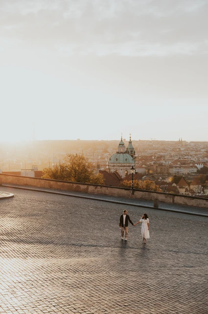 Prague anniversary photoshoot: couple holding hands above the Prague rooftops at sunrise. Couple holding hands above the Prague rooftops at sunrise during an anniversary couple photoshoot in Prague.