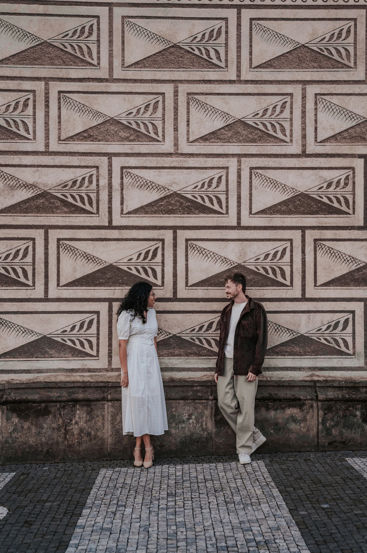 Couple holding hands against a patterned wall near Prague Castle during an anniversary couple photoshoot in Prague.