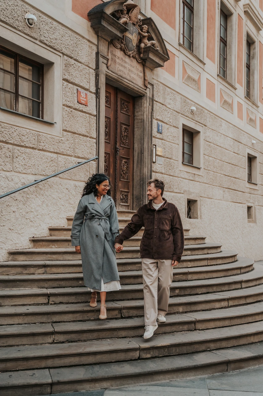 Prague anniversary photoshoot: couple holding hands while walking down steps at Prague Castle. Couple holding hands while walking down steps at Prague Castle during an anniversary couple photoshoot in Prague.
