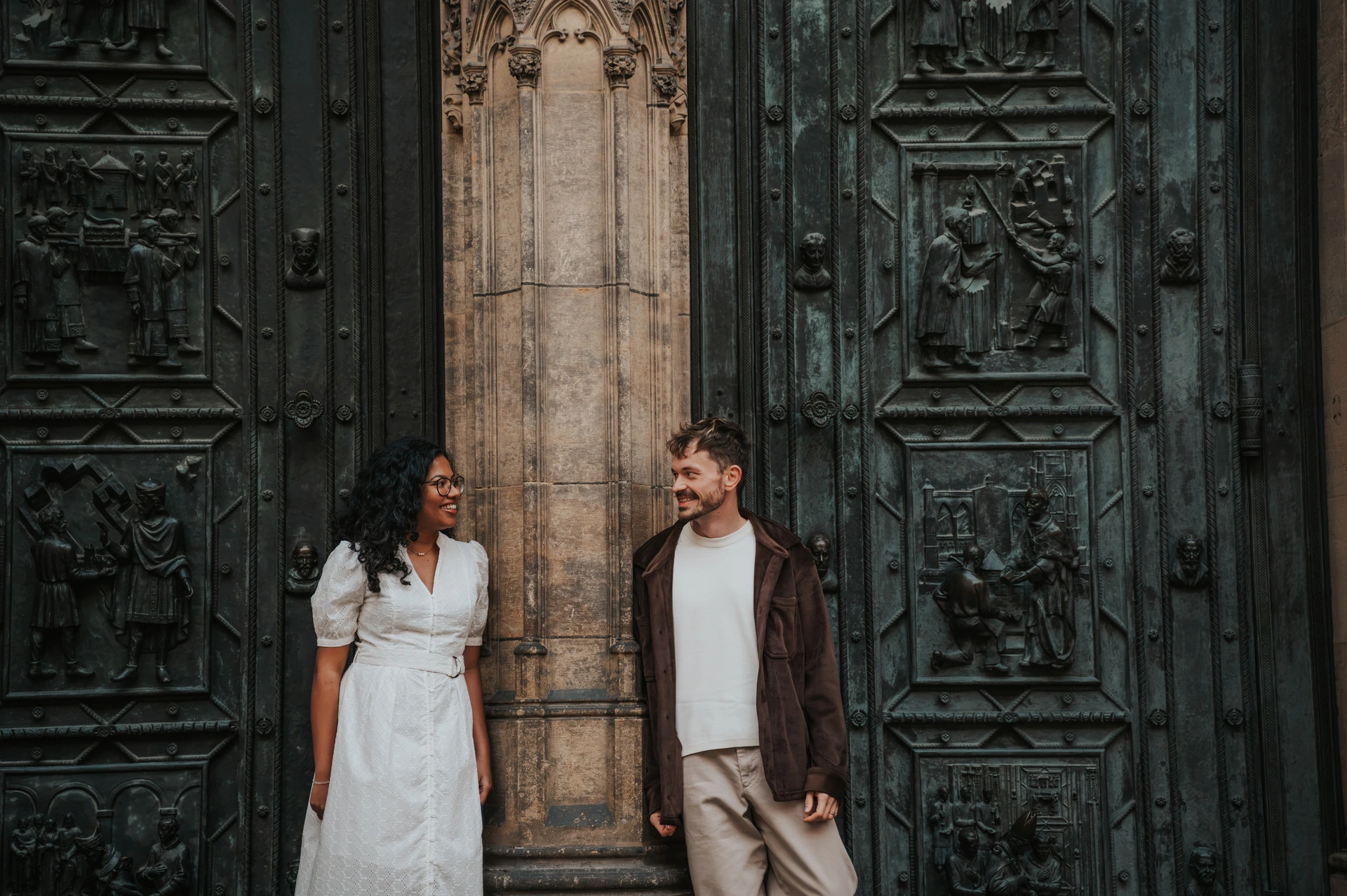 Prague anniversary photoshoot: couple smiling at each other beside the dark cathedral doors. Couple smiling at each other beside the dark cathedral doors during an anniversary couple photoshoot in Prague.