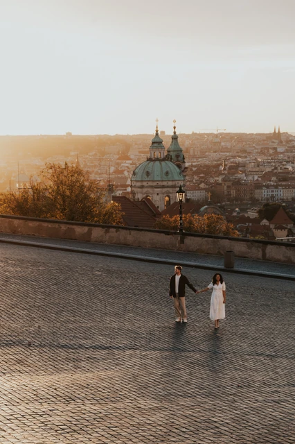 Prague anniversary photoshoot: couple standing above the city with warm morning light. Couple standing above the city with warm morning light during an anniversary couple photoshoot in Prague.