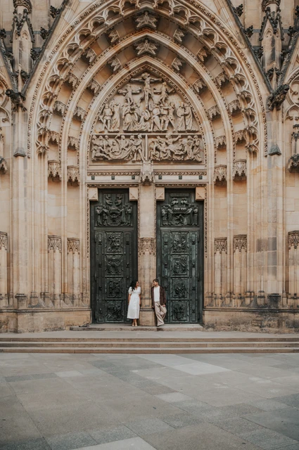 Prague anniversary photoshoot: couple standing beneath a carved cathedral arch at Prague Castle. Couple standing beneath a carved cathedral arch at Prague Castle during an anniversary couple photoshoot in Prague.