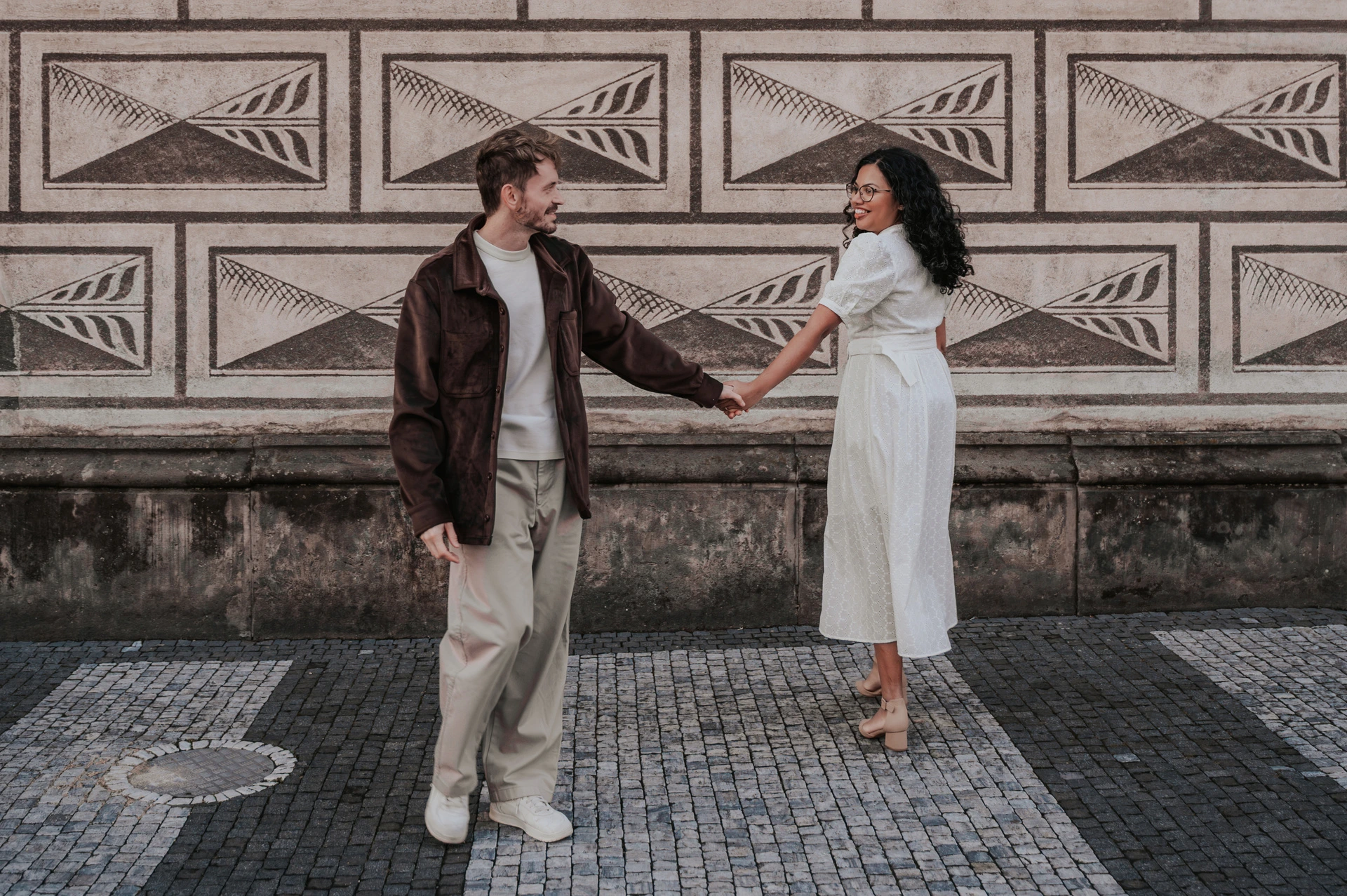Couple turning towards each other beside the patterned wall during an anniversary couple photoshoot in Prague.