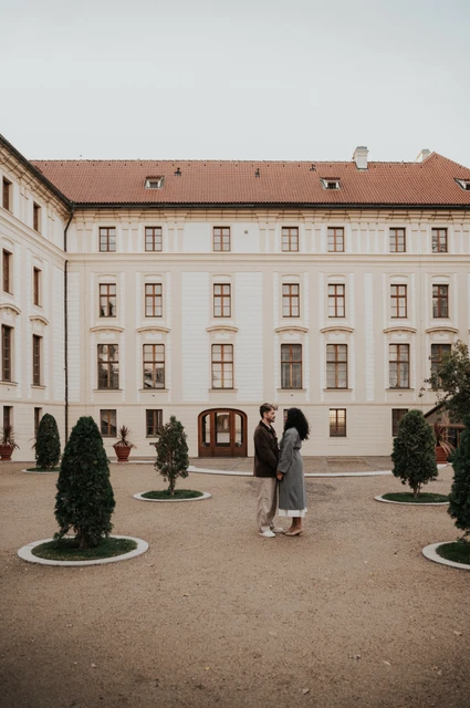 Prague anniversary photoshoot: couple walking across a quiet Prague Castle courtyard. Couple walking across a quiet Prague Castle courtyard during an anniversary couple photoshoot in Prague.