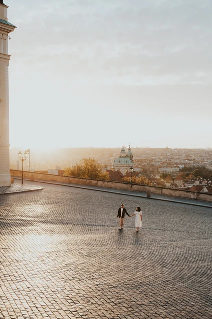 Prague anniversary photoshoot: couple walking across the open square in early sunlight. Couple walking across the open square in early sunlight during an anniversary couple photoshoot in Prague.