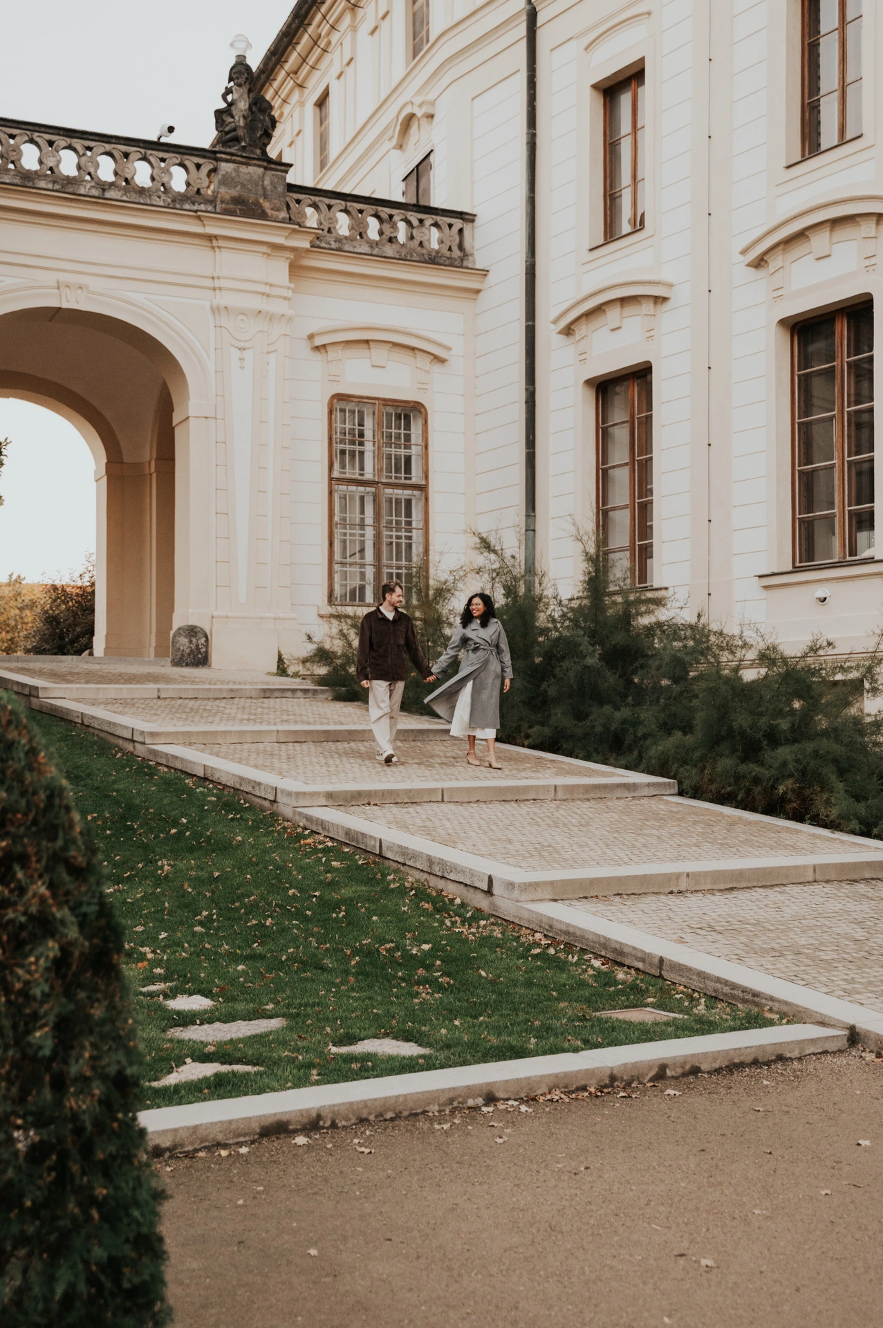 Couple walking along a path beside the castle buildings during an anniversary couple photoshoot in Prague.